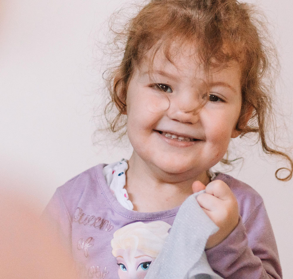 Kleines Mädchen lächelt mit ihrem Spielzeug in einem Spielzimmer.
