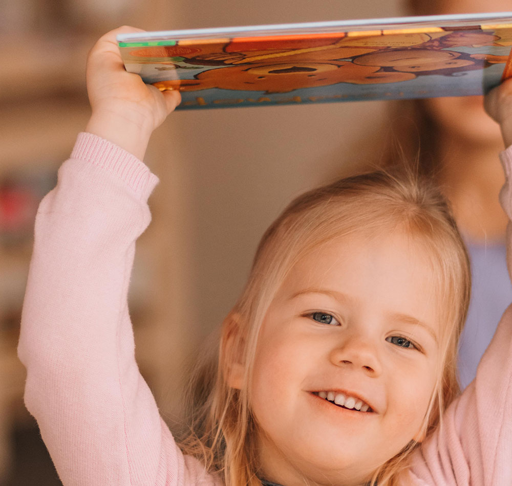 Mädchen mit einem Lächeln hebt ein buntes Buch an.