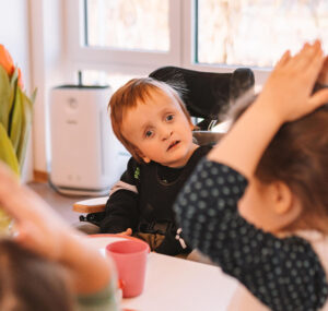 Kleiner Junge mit Behinderung sitzt am Tisch