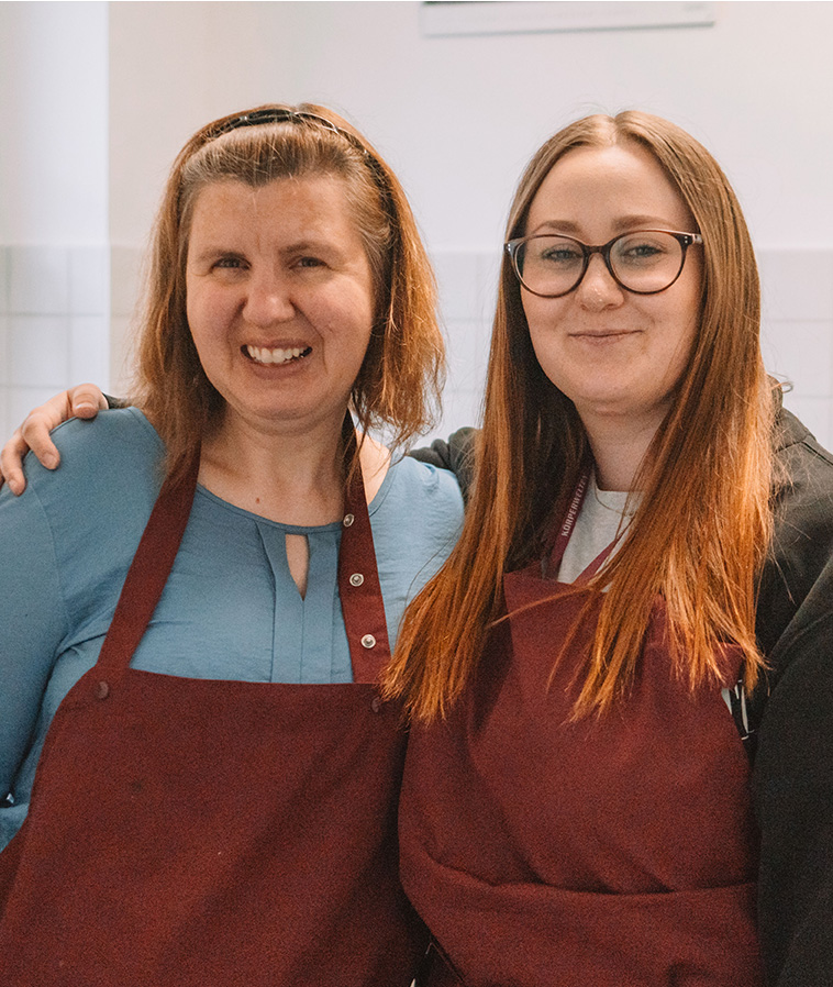 Zwei Frauen in Schürzen lächeln in der Küche