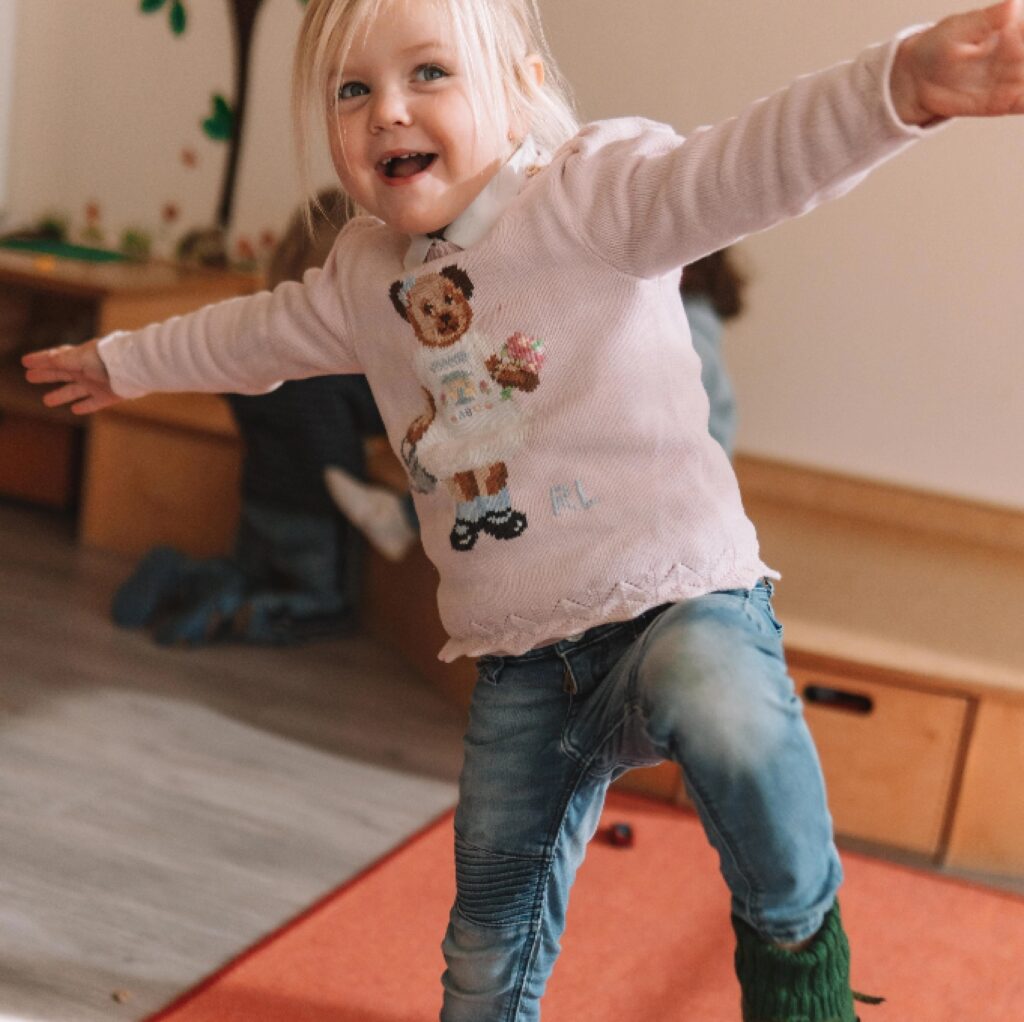 Mädchen im Pullover tanzt und lächelt im Spielzimmer.