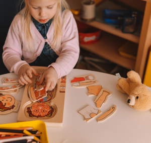 Kleines Mädchen spielt mit einem Holzpuzzle am Tisch
