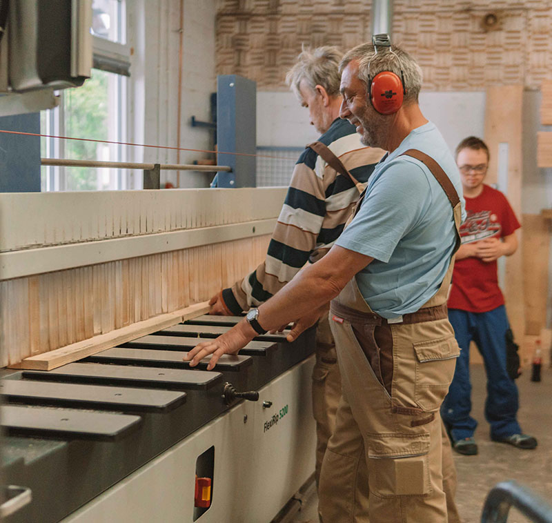 Personen arbeiten an einer Holzbearbeitungsmaschine.